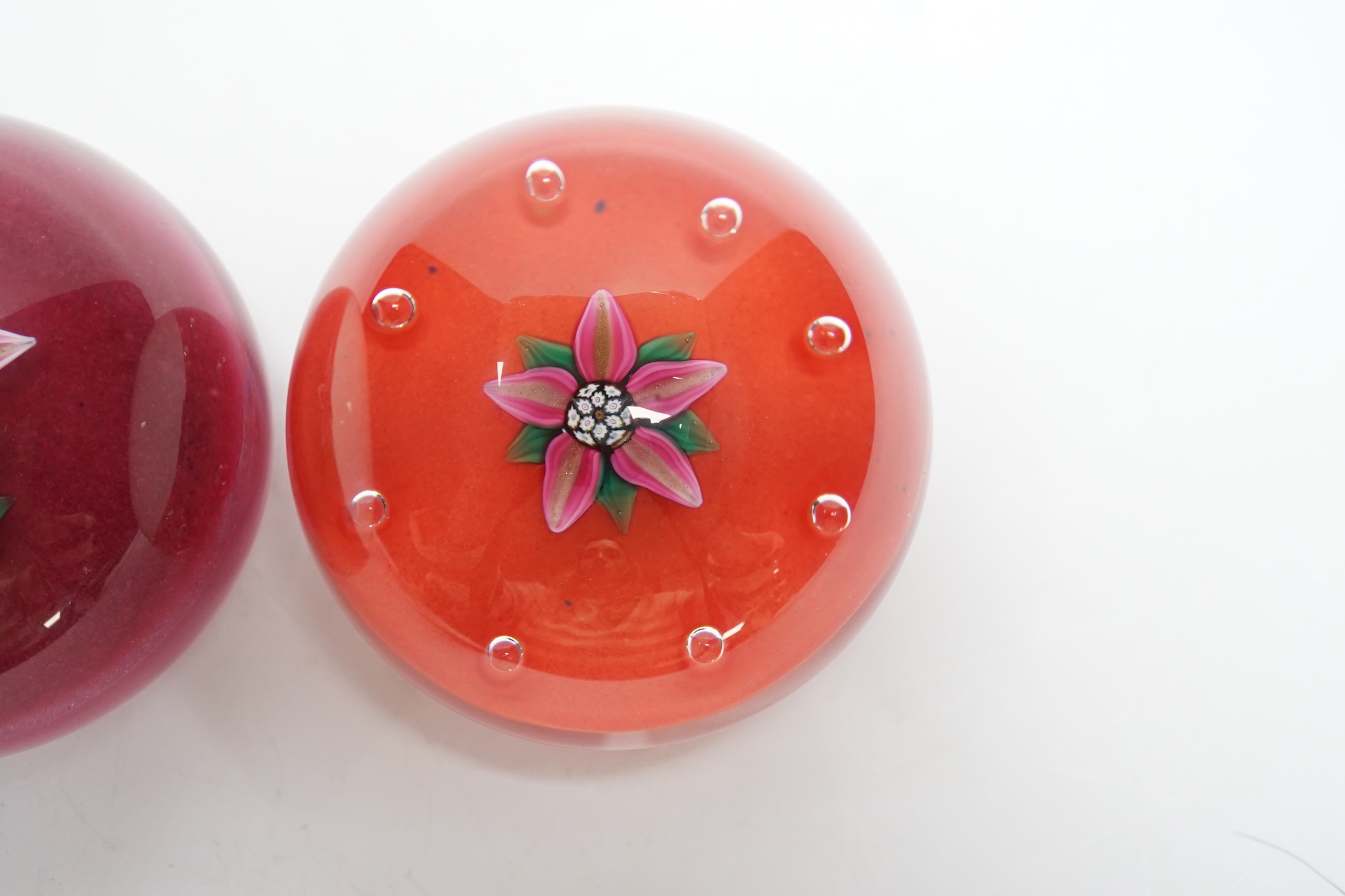 Two Paul Ysart glass ‘flower specimen’ paperweights, both Harland period, the first with a pink and aventurine flower with green stem on a raspberry ground, H cane to base, PY label, 7cm, The second with a pink and adven